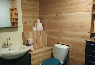 Landelijke badkamer met houten bekleding, blauw toiletdeksel en wc-papier in Emperor Bell Tent, Junora, Frankrijk.