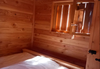 Vue intérieure d’un chalet en bois avec fenêtre ouverte et lit, au Self-sufficient, luxury eco-chalet, Camping Junora, France.