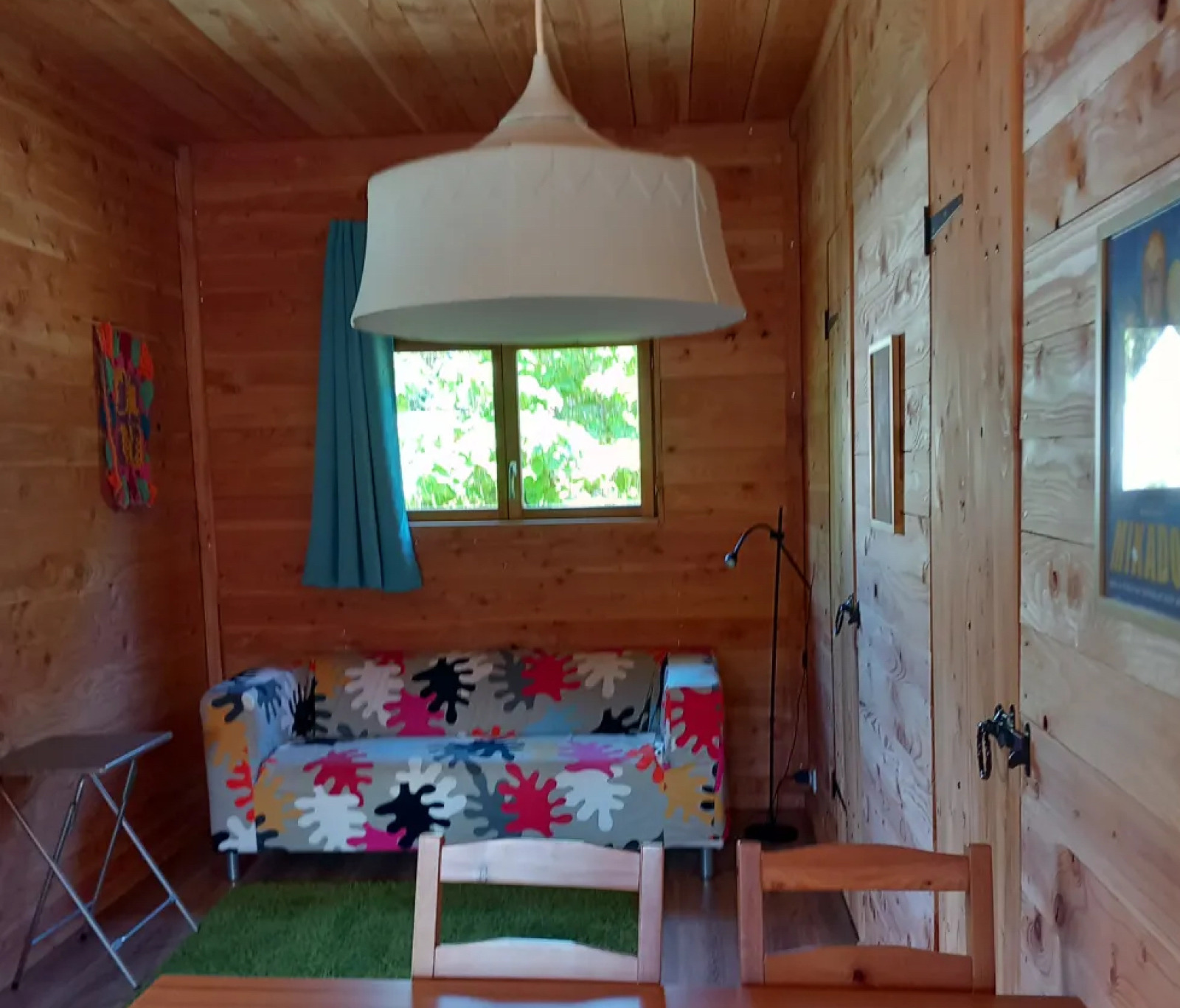 Houten interieur van een eco-chalet met kleurrijke bank en grote lamp bij Camping Junora in Frankrijk.