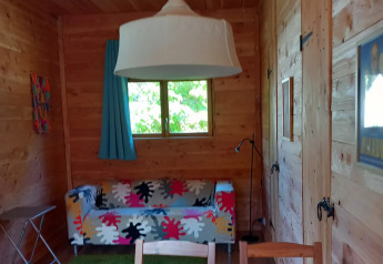 Interno in legno di un eco-chalet con divano colorato e lampada moderna al campeggio Junora in Francia.