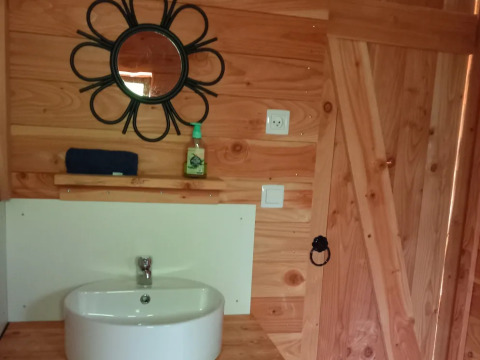 Baño con paneles de madera, lavabo, espejo circular y puerta en un lujoso eco-chalet autosuficiente.