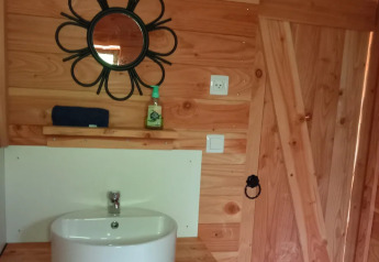 Bagno rivestito in legno con lavabo, specchio rotondo e porta in un eco-chalet di lusso autosufficiente.