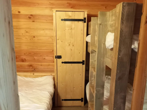 Vista interior de un chalet con literas, armario de madera y paredes de panel en Campsite Junora, Francia.