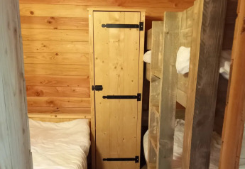 Vista interior de un chalet con literas, armario de madera y paredes de panel en Campsite Junora, Francia.