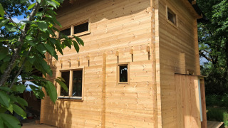 Wooden lodge named Avignon with light timber panels, surrounded by green trees and summer sunlight.