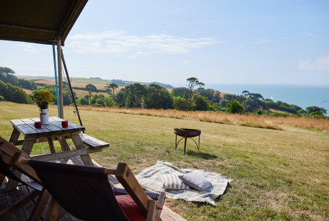 Vue depuis une tente à BoerenBed Fountain Violet Farm avec table de pique-nique, plaid et vue sur la mer, Sud-Ouest Angleterre.