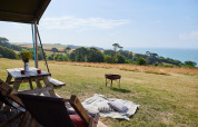Blick von einem Zelt bei BoerenBed Fountain Violet Farm mit Picknicktisch, Decke und Meerblick in Südwestengland.