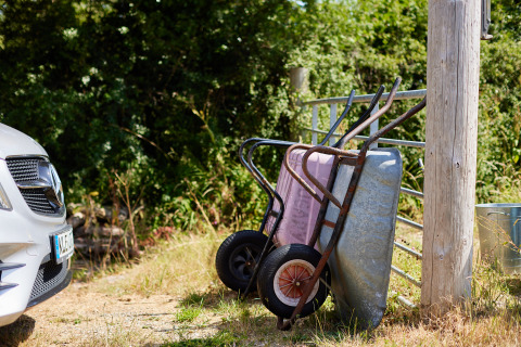 Twee kruiwagens leunen tegen een hek naast een auto bij BoerenBed Fountain Violet Farm op een zonnige dag.