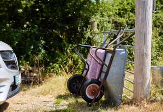Deux brouettes appuyées contre une barrière à côté d’une voiture à BoerenBed Fountain Violet Farm, en plein soleil.