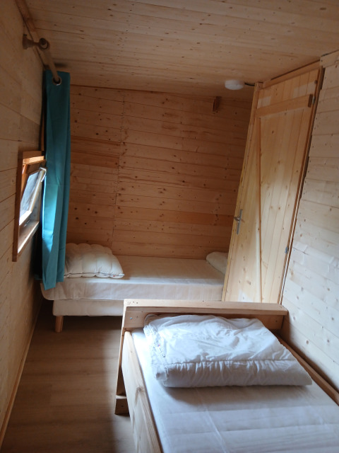 Stanza in legno con due letti singoli e tenda blu nel lodge «Avignon» al Campeggio Junora, Francia.