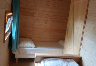 Stanza in legno con due letti singoli e tenda blu nel lodge «Avignon» al Campeggio Junora, Francia.