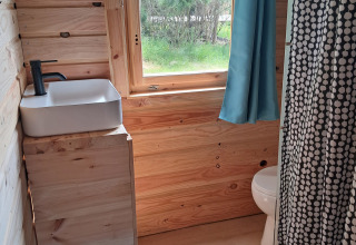 Bagno compatto in legno alla lodge Avignon, Campsite Junora, finestra luminosa e tappeto blu.