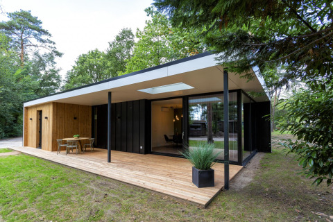 Lodge Forest Cottage moderna con terrazza in legno, ampie vetrate e area esterna tra gli alberi del bosco.