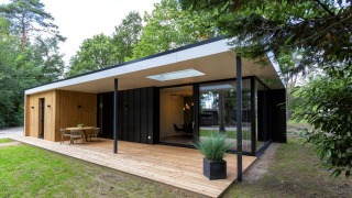 Lodge Forest Cottage moderne avec terrasse en bois, grandes baies vitrées et nature environnante verdoyante.