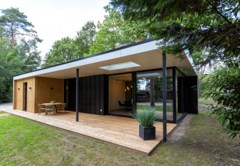 Lodge Forest Cottage moderno con terraza de madera, ventanales y comedor exterior rodeado de naturaleza.