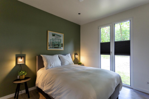 Chambre moderne au Forest Cottage au Holiday Park BreeBronne, Pays-Bas, avec mur vert et lit double.