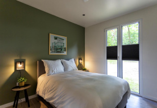 Dormitorio moderno en Forest Cottage, Holiday Park BreeBronne, Países Bajos, con pared verde y cama.