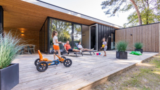 Familie hygger sig på træterrasse foran Forest Cottage, med børn der leger og voksne der slapper af.