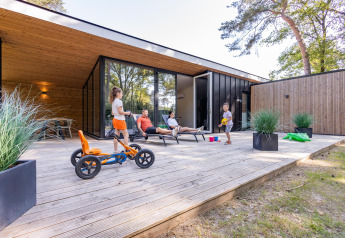 Familie entspannt auf der Holzterrasse der Forest Cottage, Kinder spielen fröhlich im Außenbereich.