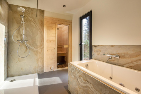 Helles Bad mit Dusche, Badewanne und Sauna im Forest Cottage im Ferienpark BreeBronne, Niederlande.