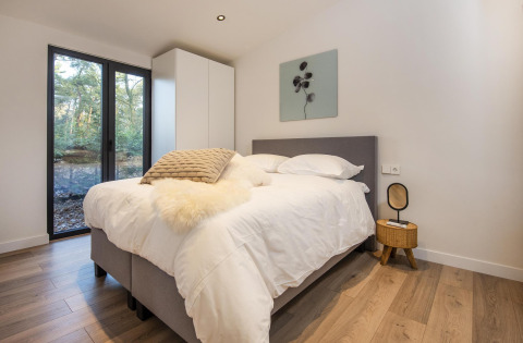 Moderne soveværelse med stor seng, store vinduer og udsigt til skov i Forest Cottage, BreeBronne, Holland.