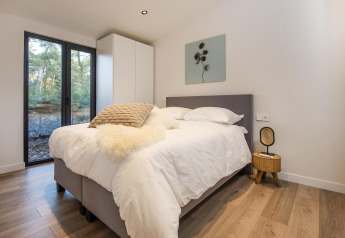 Dormitorio moderno con cama grande, ventanas amplias y vista al bosque en Forest Cottage, BreeBronne, Países Bajos.