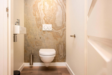 Modern restroom with wall-mounted toilet, small sink, and marble wall at Forest Cottage, BreeBronne, Netherlands.
