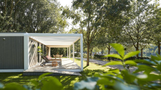 Terrazza esterna alla Forest Cube lodge con sdraio e tavolo, circondata da alberi verdi e natura.