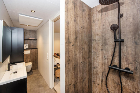 Baño moderno en Forest Cube, Holiday Park BreeBronne, Países Bajos, con paredes de madera y ducha negra.