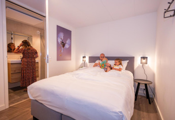 Familie entspannt im Schlafzimmer der Forest Cube Lodge im Ferienpark BreeBronne, Niederlande.