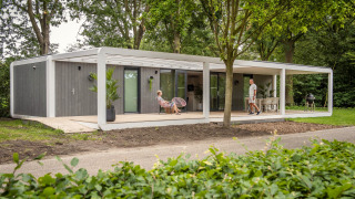 Moderne Forest Cube lodge i skoven med brede terrasser, udendørs siddeplads og to personer i ro.