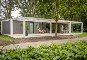 Lodge Forest Cube contemporain au milieu des arbres, grande terrasse, salon extérieur et deux personnes détendues.