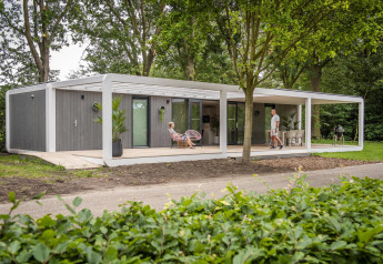 Moderne Forest Cube Lodge im Grünen mit großer Veranda, Sitzbereich im Freien und zwei Personen.
