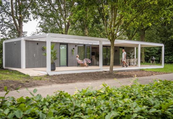 Moderne Forest Cube lodge i skoven med brede terrasser, udendørs siddeplads og to personer i ro.