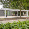 Moderne Forest Cube lodge i skoven med brede terrasser, udendørs siddeplads og to personer i ro.