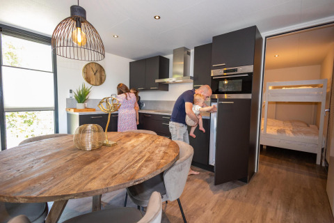 Gezin geniet samen in een moderne keuken in de Forest Cube lodge bij Holiday Park BreeBronne, Nederland.