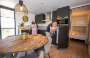 Gezin geniet samen in een moderne keuken in de Forest Cube lodge bij Holiday Park BreeBronne, Nederland.