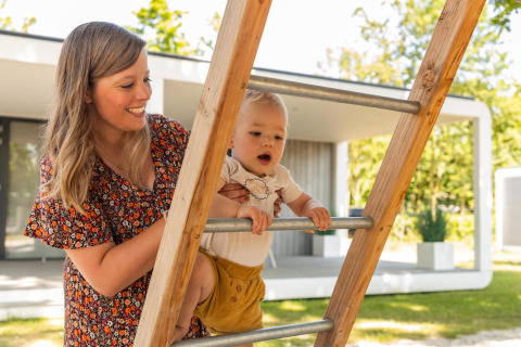 Een moeder helpt haar kind een houten ladder op bij de Forest Cube-lodge in Holiday Park BreeBronne in Nederland.