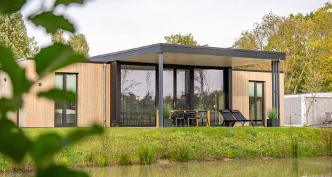 Moderne houten Forest Lodge aan de vijver, met terrasmeubilair en loungestoelen, omgeven door natuur.