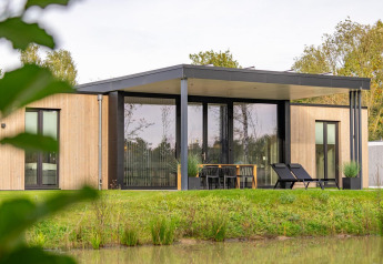 Modern wooden Forest Lodge by the pond, featuring a covered patio, outdoor seating, and scenic greenery.