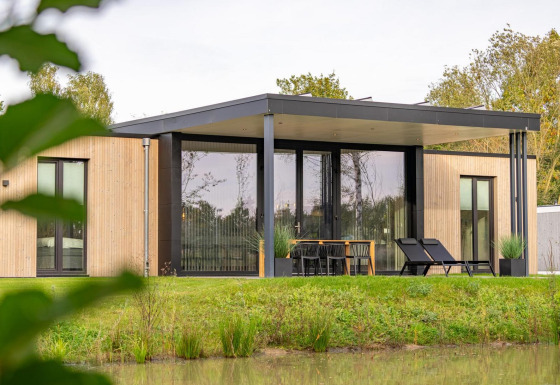 Moderne houten Forest Lodge aan de vijver, met terrasmeubilair en loungestoelen, omgeven door natuur.