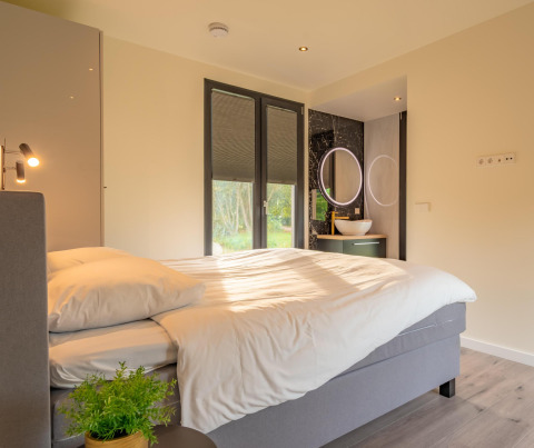 Gezellige slaapkamer in Forest Lodge van Holiday Park BreeBronne, Nederland, met groot bed en moderne badkamer.