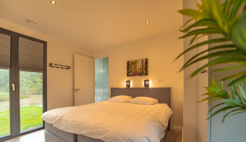 Slaapkamer met tweepersoonsbed, modern ingericht en grote ramen in Forest Lodge, BreeBronne, Nederland.