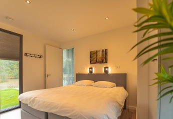 Chambre avec lit double, décor moderne et grandes fenêtres à Forest Lodge, BreeBronne, Pays-Bas.