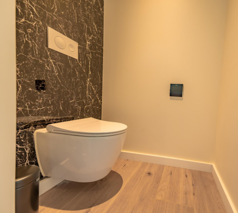 Moderne toiletruimte met hangtoilet, zwarte marmeren wand en houten vloer in Forest Lodge, BreeBronne.