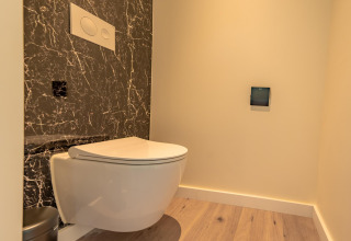Moderne toiletruimte met hangtoilet, zwarte marmeren wand en houten vloer in Forest Lodge, BreeBronne.