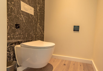 Baño moderno con inodoro suspendido, panel de mármol negro y suelo de madera en Forest Lodge, BreeBronne.