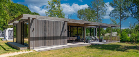 Lodge Forest Villa à façade bois moderne, grande terrasse couverte, entourée d'arbres et de verdure.