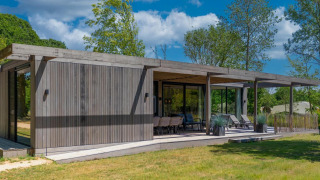 Lodge Forest Villa à façade bois moderne, grande terrasse couverte, entourée d'arbres et de verdure.