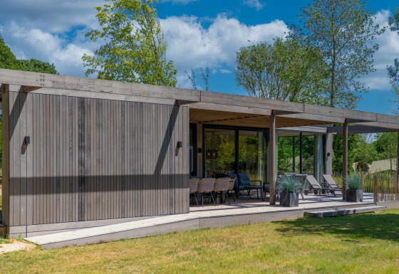 Forest Villa lodge con fachada moderna de madera, terraza grande y rodeada de árboles y césped verde.
